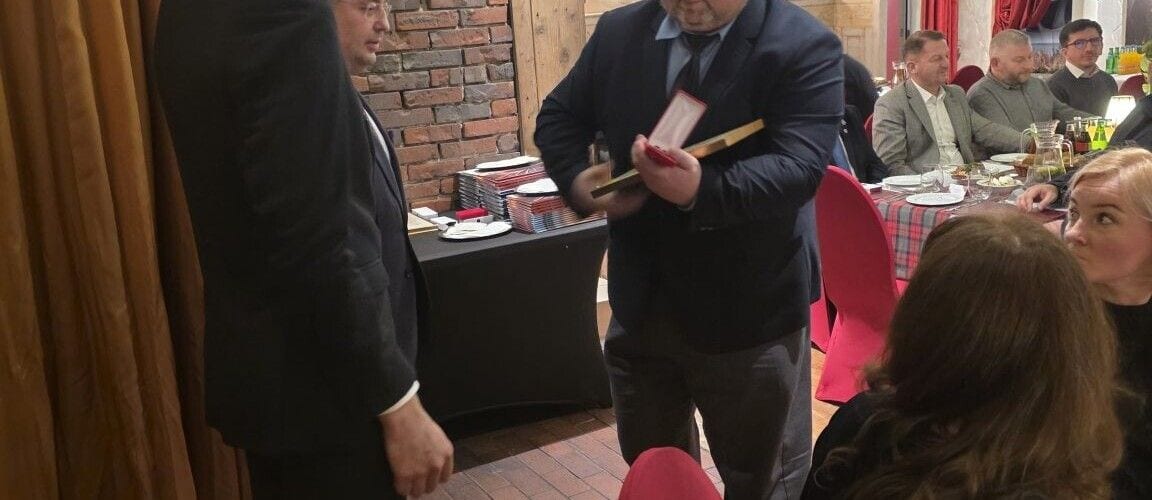 Mężczyzna prezentujący otwarte etui z medalem podczas uroczystego spotkania.