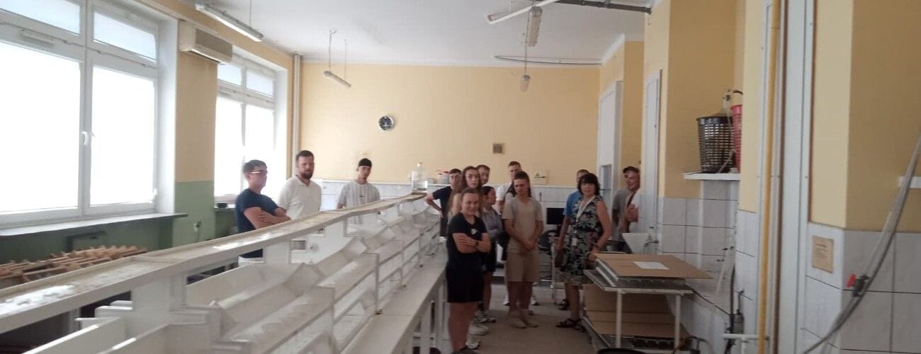 Grupa uczestników wizyty w jasnym laboratorium z długimi stołami roboczymi.