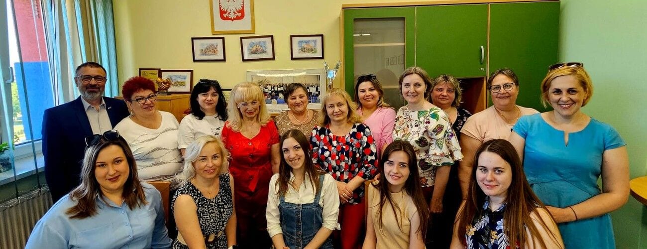 Delegacja i gospodarze wizyty pozujący w sali uczelni na tle tablicy i godła Polski.