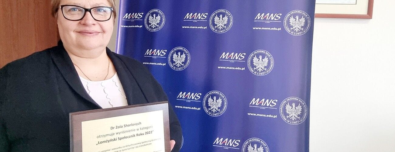 Laureatka wyróżnienia prezentująca dyplom na tle ścianki MANS.