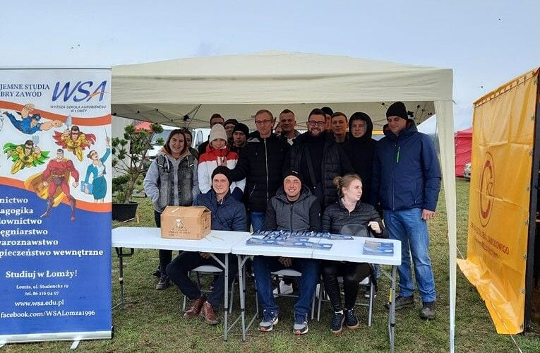 Przedstawiciele uczelni przy stoisku promocyjnym pod namiotem na targach ogrodniczych.
