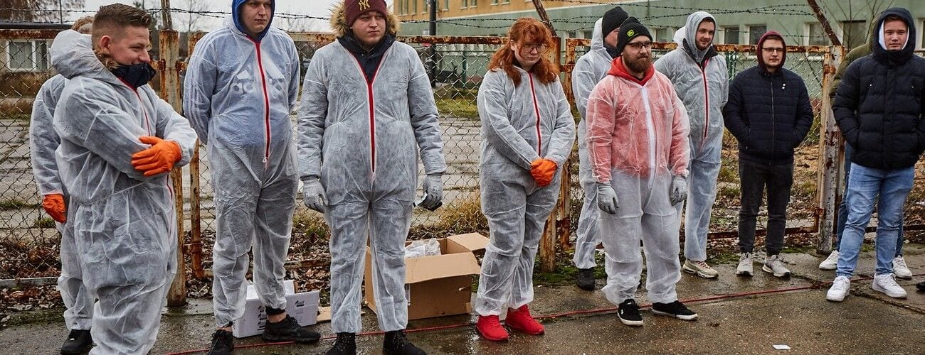 Uczestnicy projektu ProCare w białych kombinezonach ochronnych i pomarańczowych rękawicach w tunelu uprawowym.