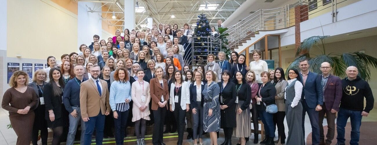 Liczna grupa uczestników sympozjum dziekanatów pozująca na schodach wewnątrz uczelni.