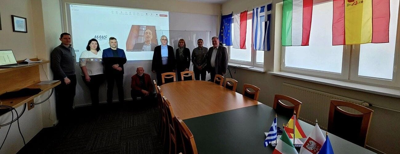 Uczestnicy inauguracji In4Aut w sali konferencyjnej z flagami państw partnerskich.