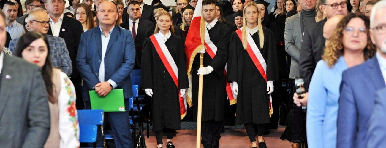 Poczet sztandarowy i goście stojący podczas inauguracji roku akademickiego.
