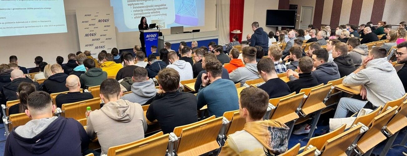 Uczestnicy w wypełnionej sali wykładowej podczas wystąpienia przy mównicy MANS.