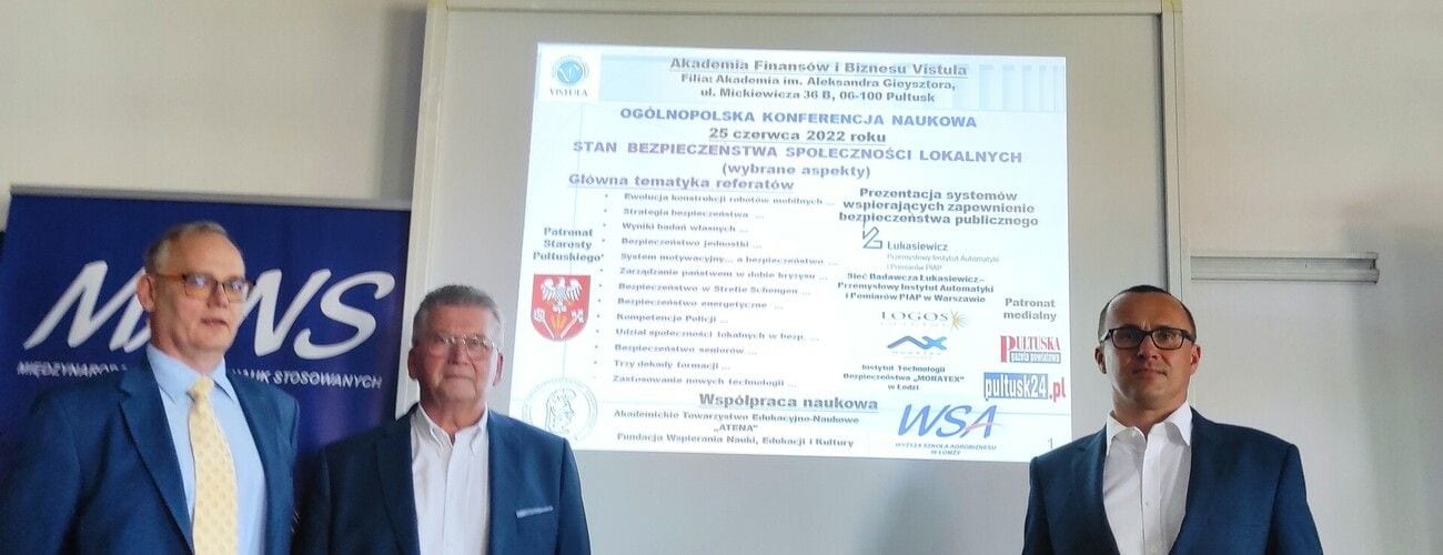 Trzej uczestnicy konferencji przed ekranem z programem dotyczącym bezpieczeństwa społeczności lokalnych.