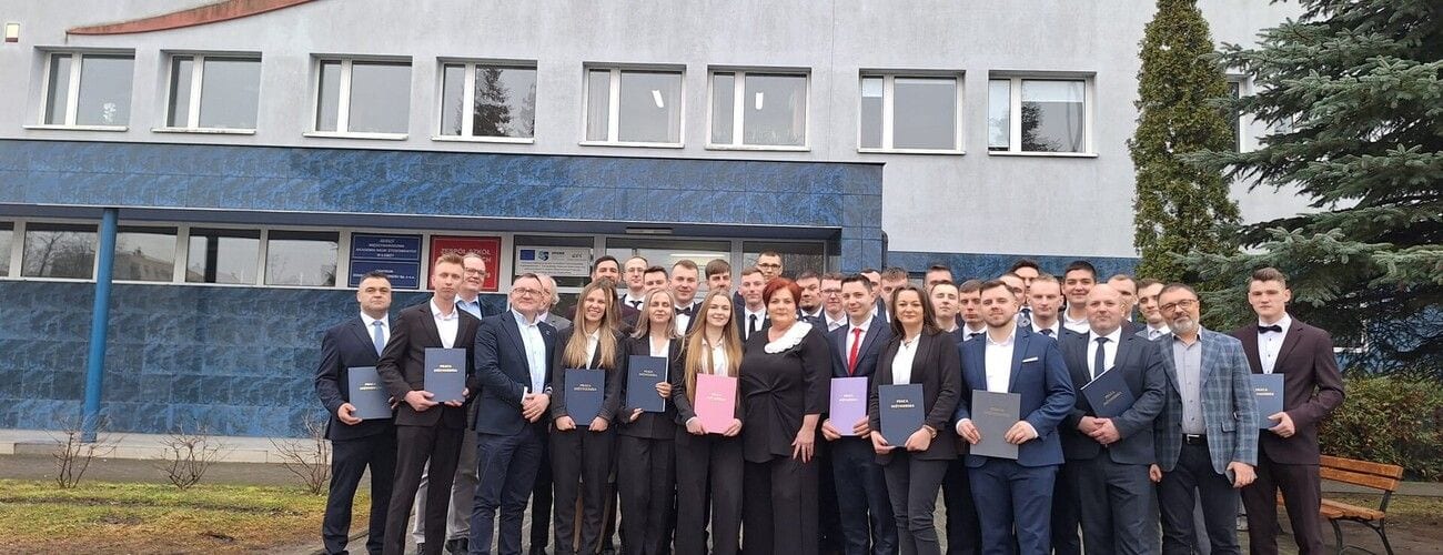Absolwenci prezentujący dyplomy wraz z przedstawicielami uczelni przed budynkiem MANS.