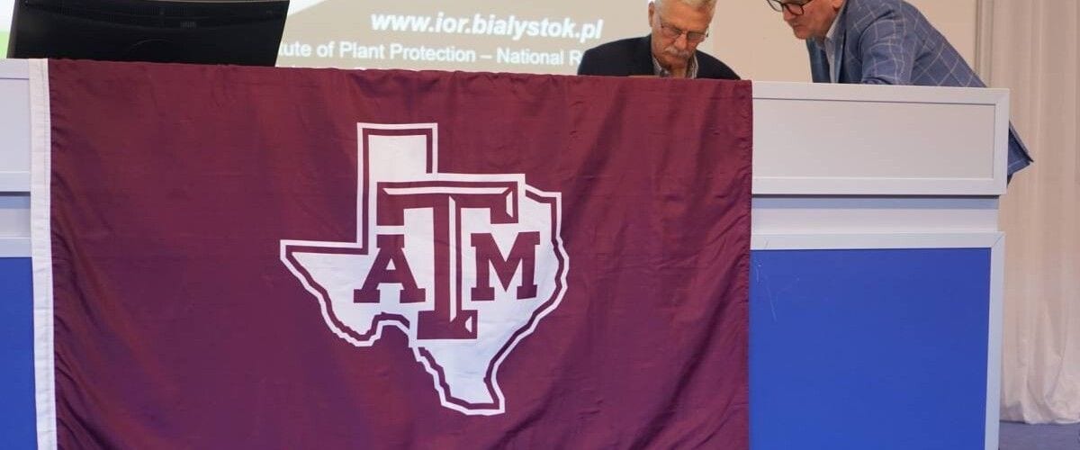 Bordowa flaga Texas A&M wywieszona przy mównicy uczelni podczas spotkania.