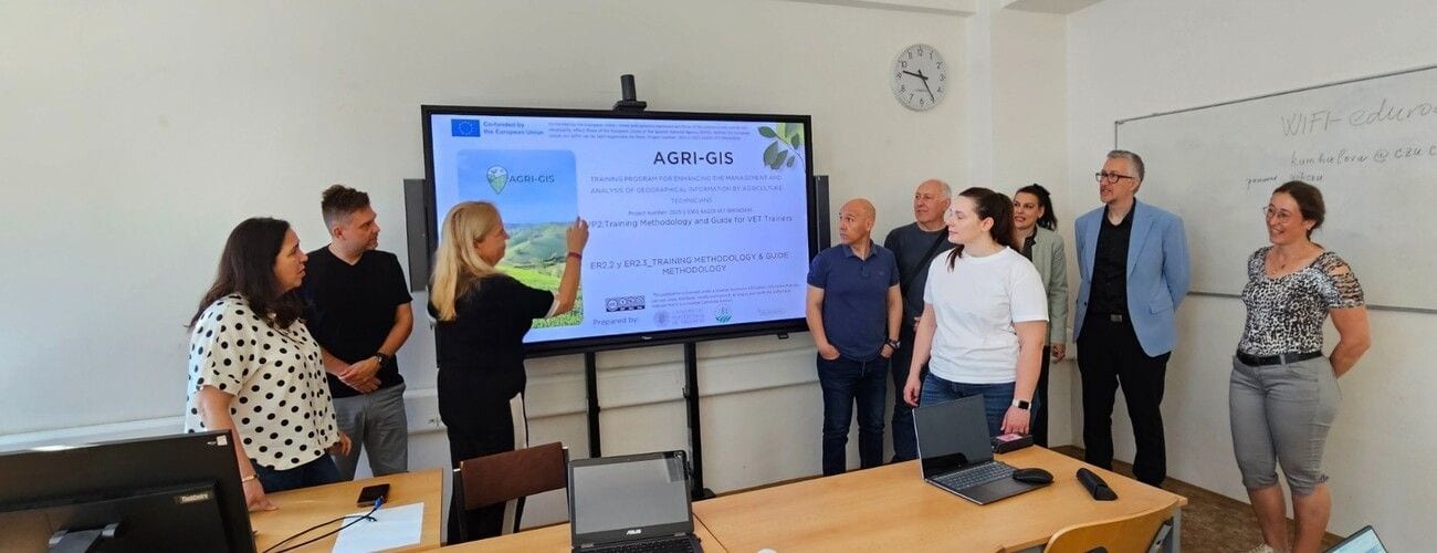 Uczestnicy spotkania przy ekranie z prezentacją AGRI-GIS; jedna z osób wskazuje element slajdu.