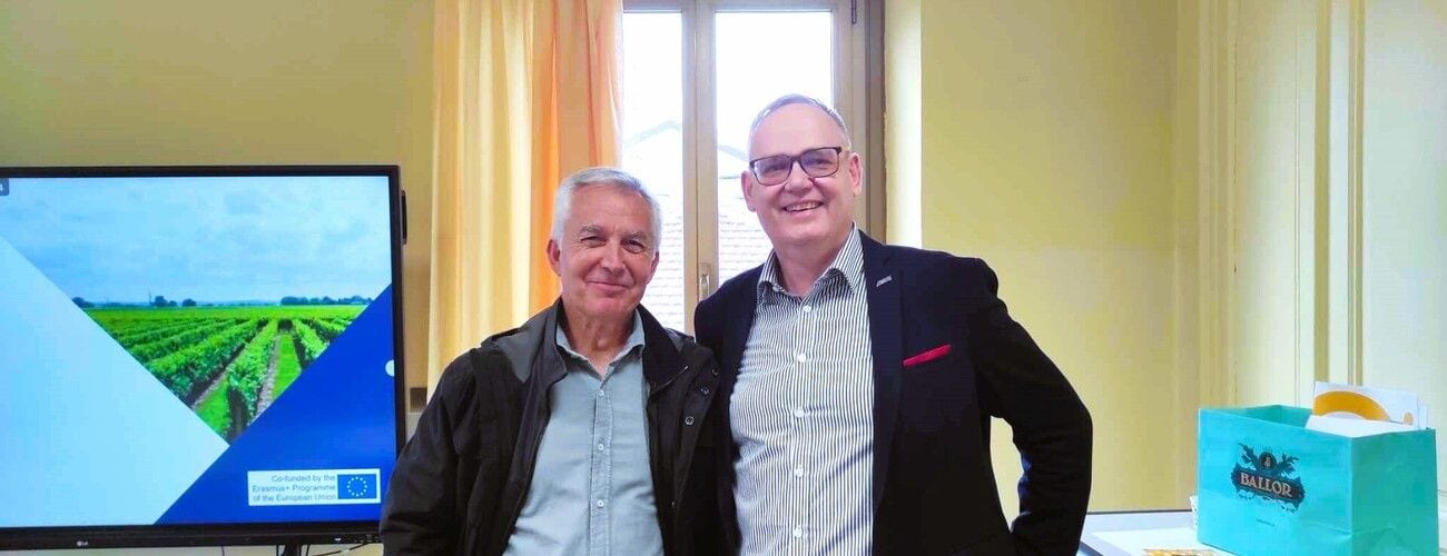Dwaj uczestnicy spotkania akademickiego pozujący obok ekranu ze zdjęciem upraw.
