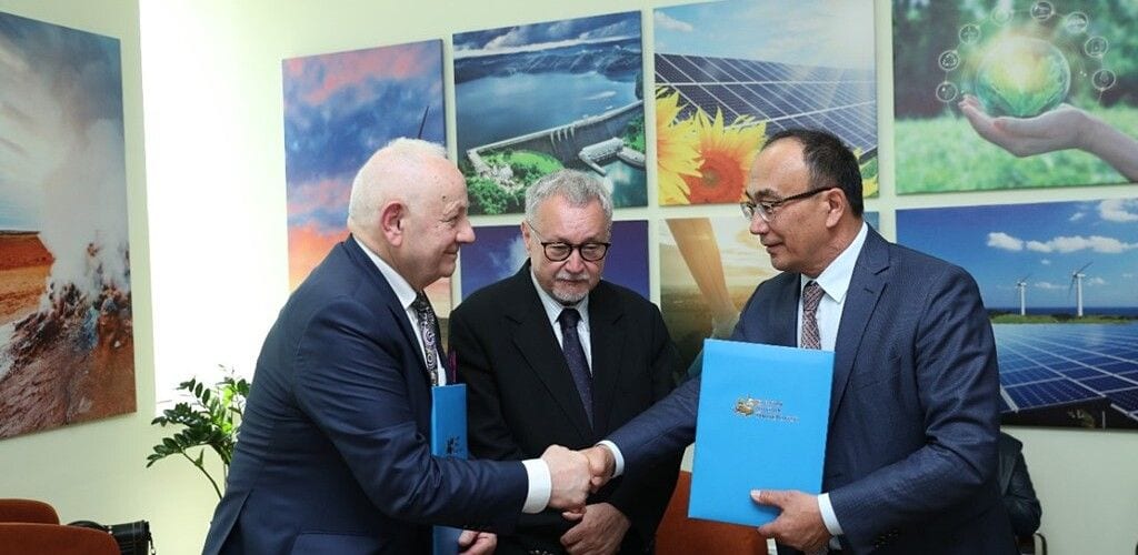 Uścisk dłoni podczas otwarcia Centrum Badawczego „Zielona Gospodarka”, na tle zdjęć energii odnawialnej.