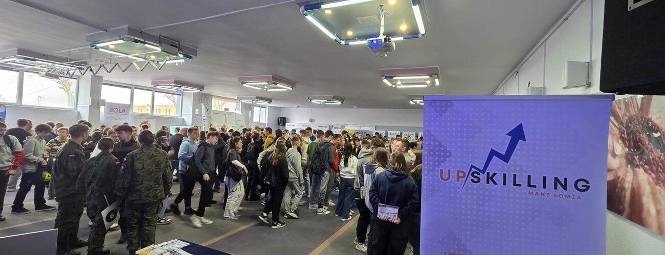 Uczestnicy panelu edukacyjnego w zatłoczonej auli, obok plansza projektu UPSKILLING.