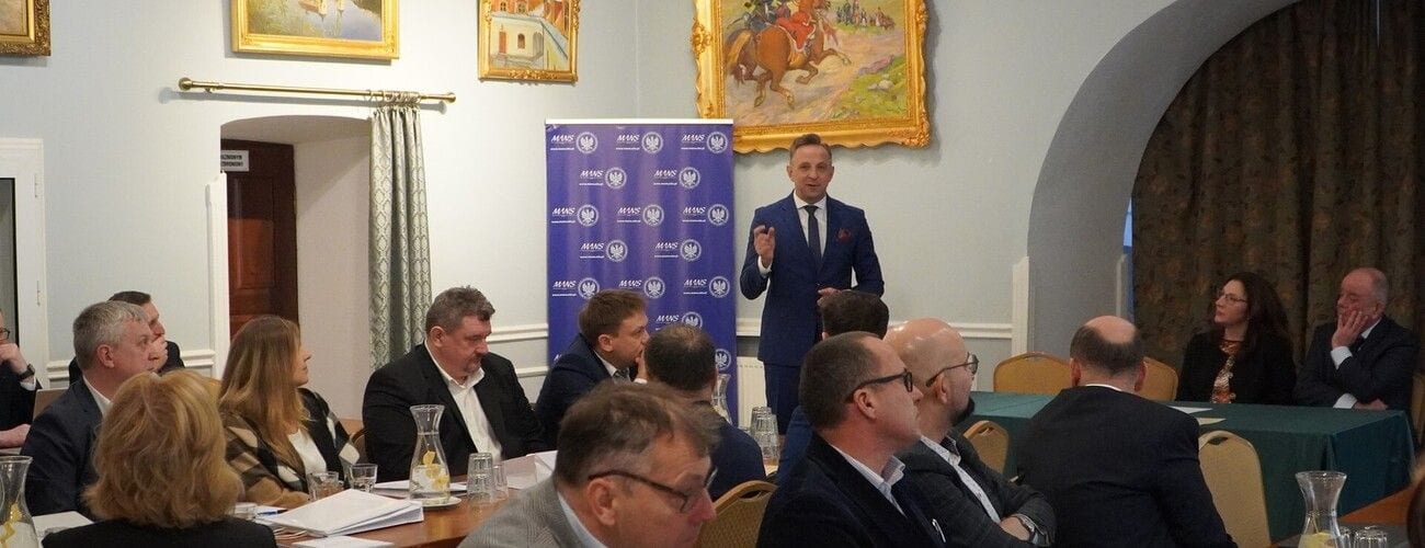 Dyskusja uczestników konferencji przy stołach w sali z obrazami na ścianach.