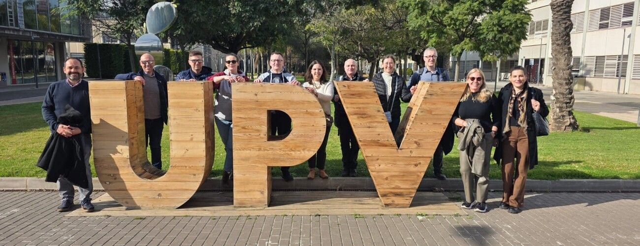 Uczestnicy spotkania AGRI-GIS przy dużych drewnianych literach UPV na zielonym terenie kampusu.