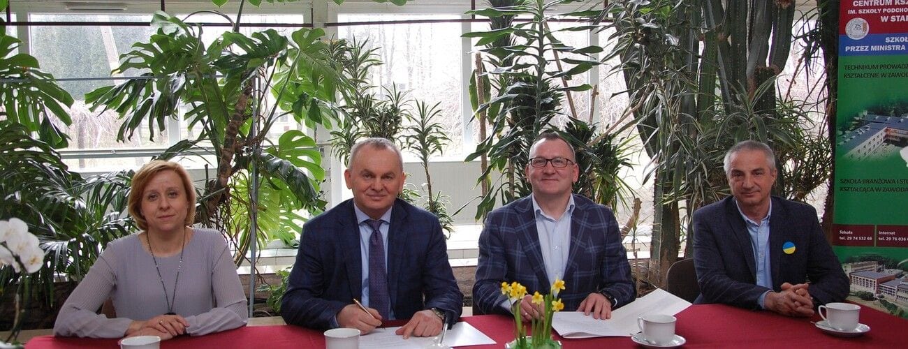 Cztery osoby przy stole z dokumentami podczas spotkania poświęconego współpracy uczelni ze szkołą.