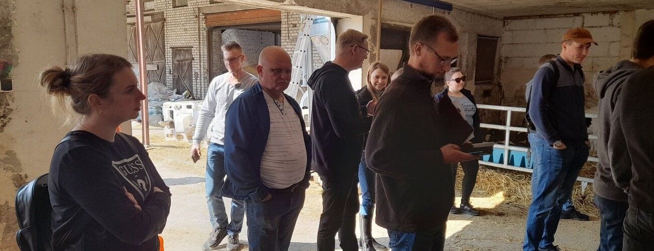 Grupa zwiedzająca wnętrze obory podczas zajęć poświęconych nowoczesnej produkcji mleka.