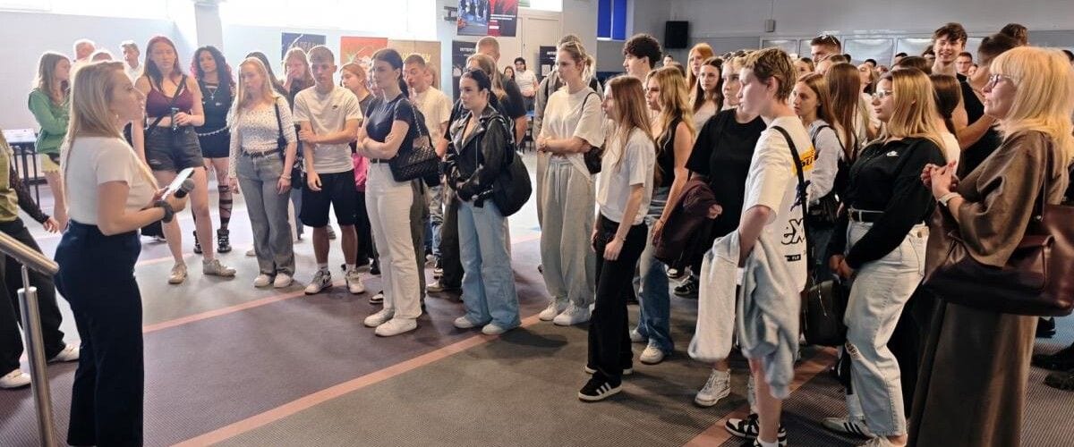 Młodzi uczestnicy dnia otwartego słuchający prowadzącej w sali uczelni.
