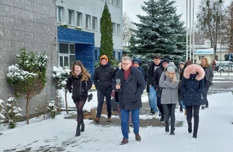 Uczestnicy szkolenia z kamerą termowizyjną przed budynkiem uczelni w zimowej scenerii.