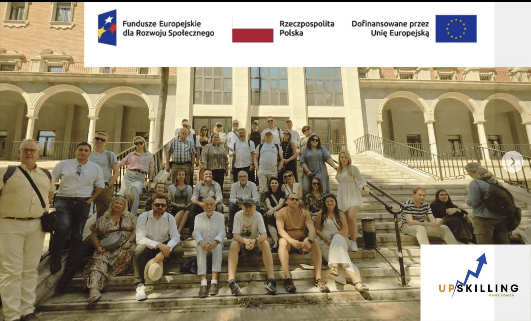 Uczestnicy wyjazdu UPSKILLING pozują na schodach przed budynkiem; na zdjęciu logotypy finansowania i projektu.