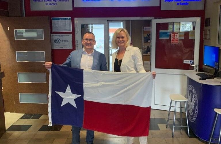 Dwie osoby trzymające flagę Teksasu podczas wizyty delegacji ACDS na uczelni.
