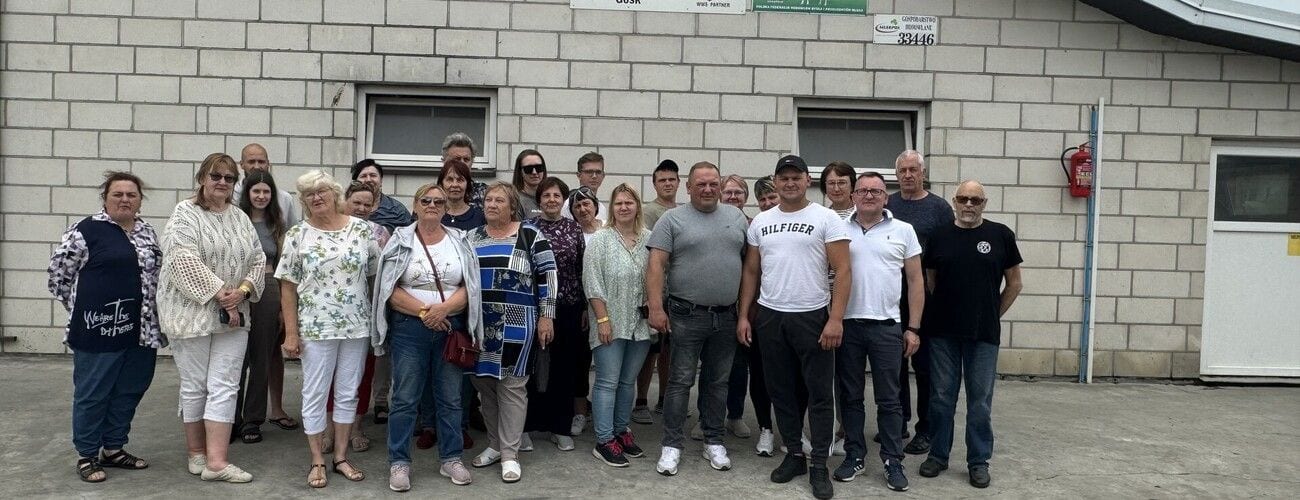 Goście i gospodarze wizyty z Łotwy pozujący przed murowanym budynkiem.