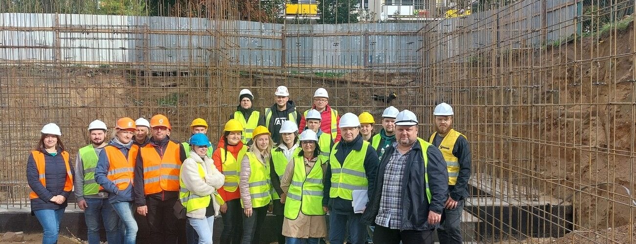 Studenci w kaskach i kamizelkach odblaskowych na budowie, na tle zbrojenia ścian.
