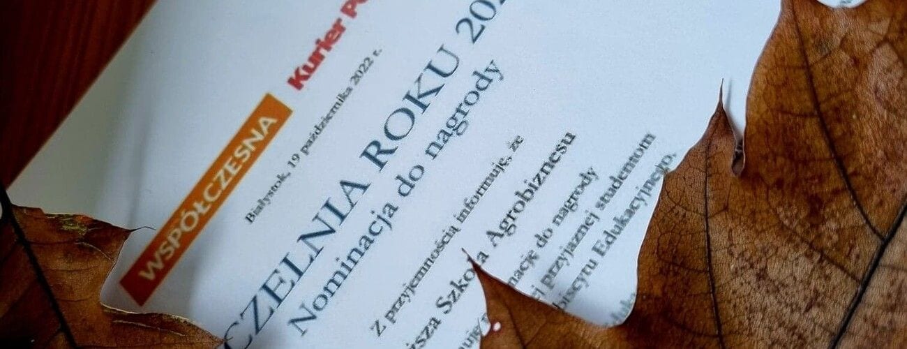 Dyplom nominacji do nagrody „Uczelnia Roku” częściowo otoczony jesiennymi liśćmi.