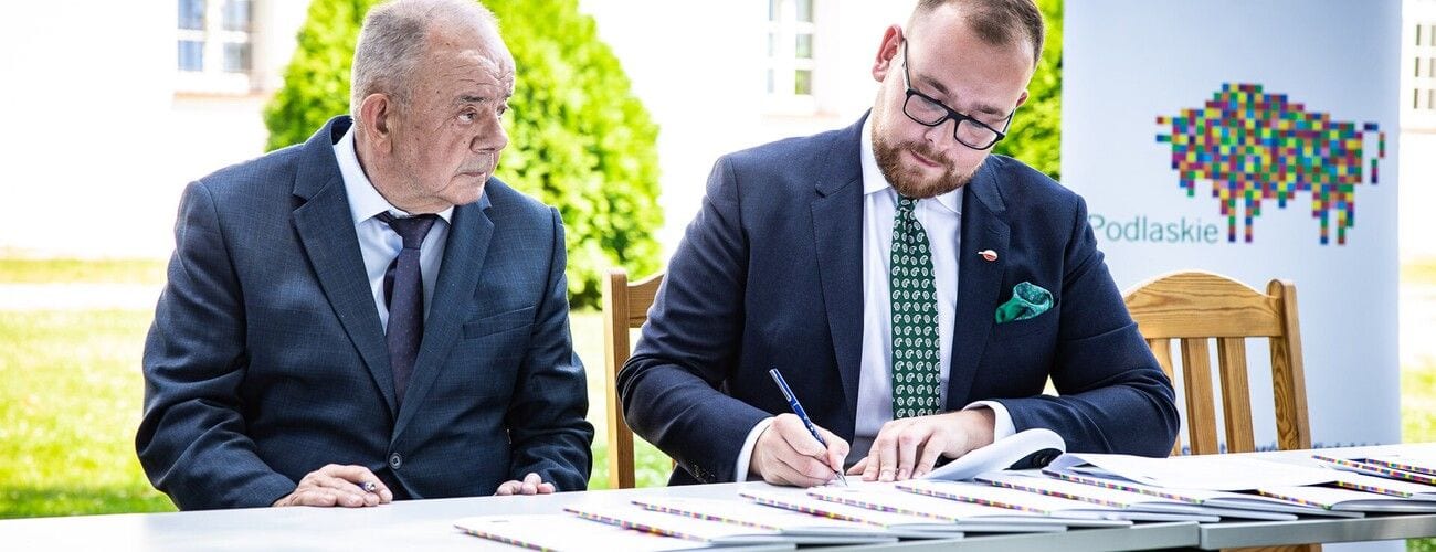Dwaj przedstawiciele instytucji przy stole podczas podpisywania dokumentów współpracy.