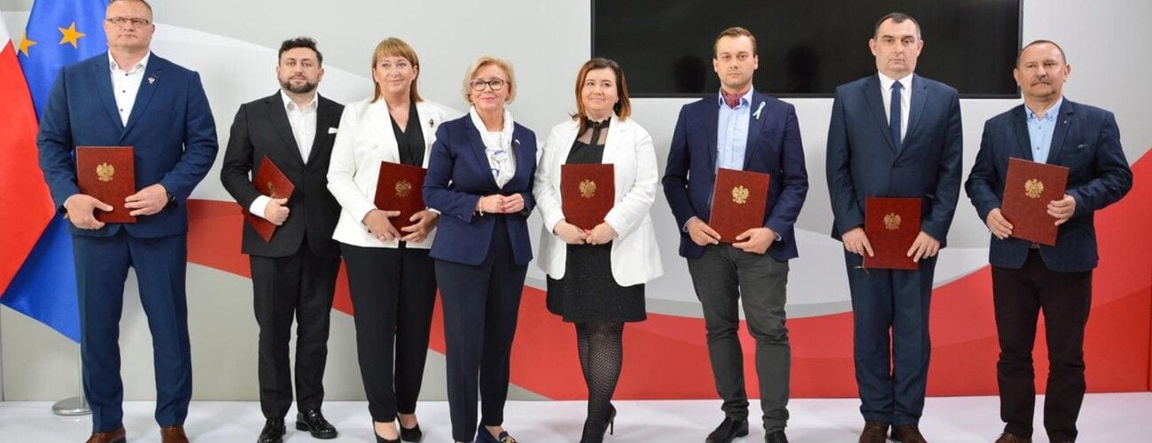 Uczestnicy uroczystości wręczenia wyróżnień pozujący z czerwonymi teczkami dyplomów.