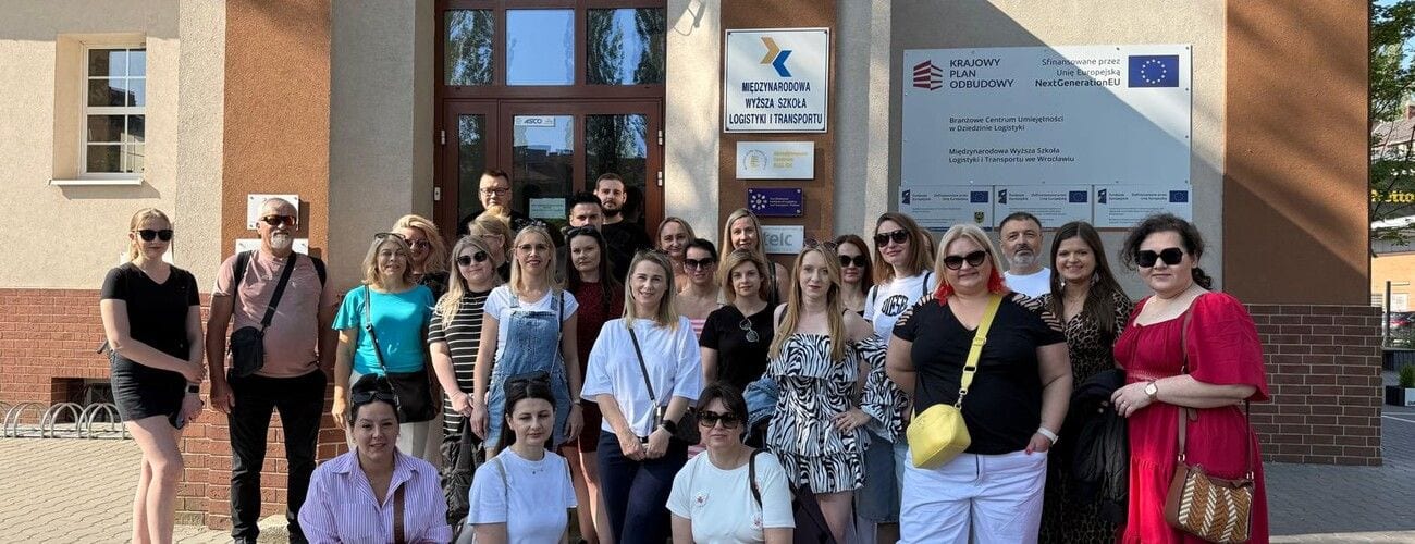 Uczestnicy wyjazdu do Wrocławia pozujący przed wejściem do budynku z tablicami informacyjnymi.