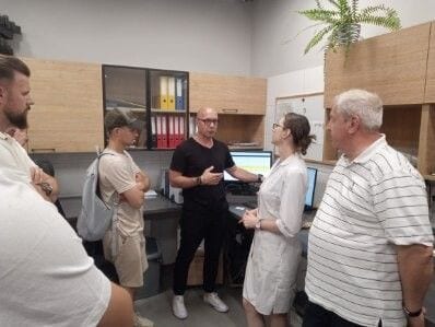 Niewielka grupa podczas rozmowy w pomieszczeniu laboratoryjnym, przy komputerze i półkach z dokumentacją.