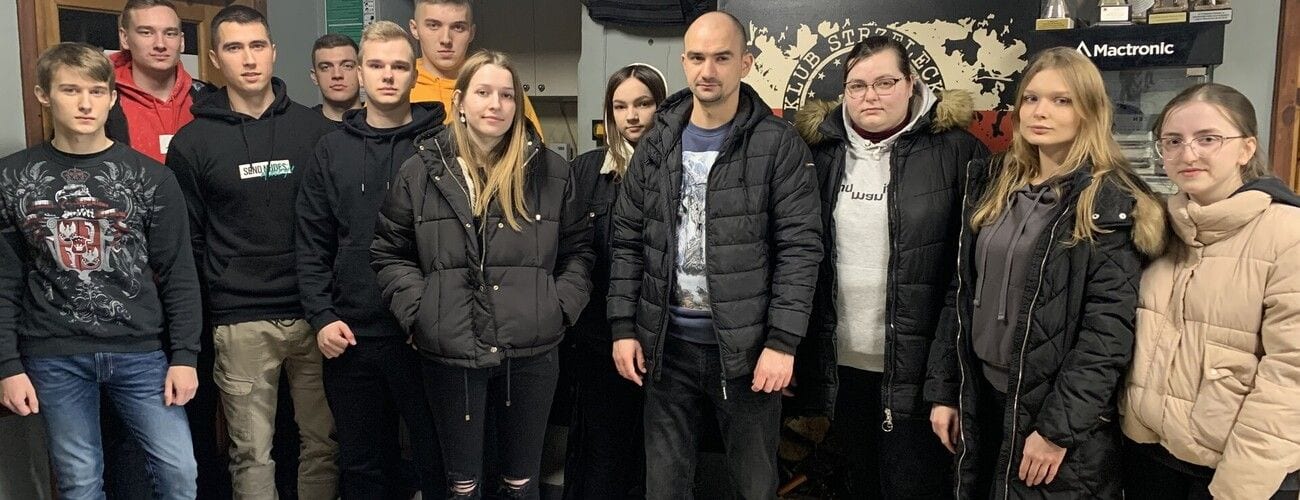 Grupa studentów i prowadzących pozująca we wnętrzu obiektu szkoleniowego.