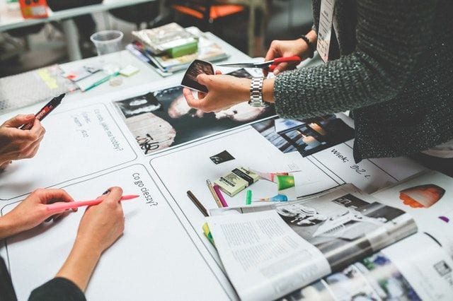 Grupa osób pracuje przy stole nad wydrukami i projektami.