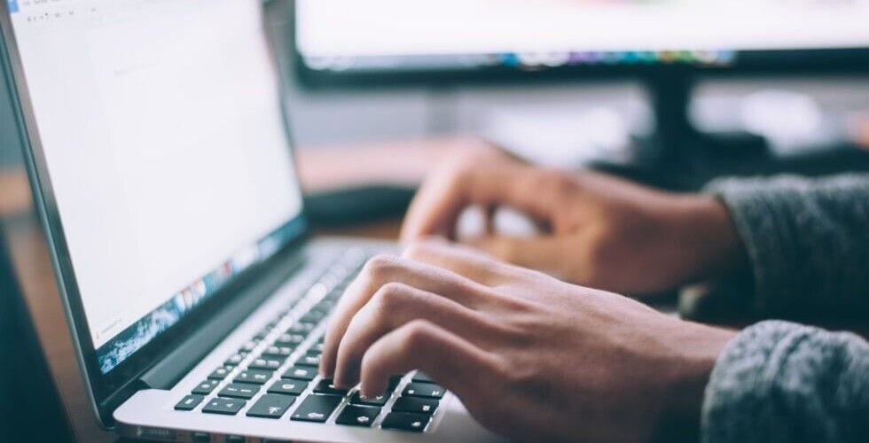 Zbliżenie dłoni piszących na klawiaturze laptopa.